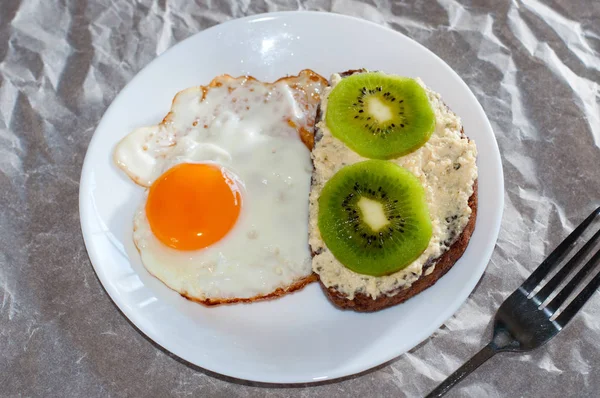 Delicioso e saudável café da manhã. Ovos fritos e sanduíche de kiwi em um prato branco, close-up, espaço para texto — Fotografia de Stock