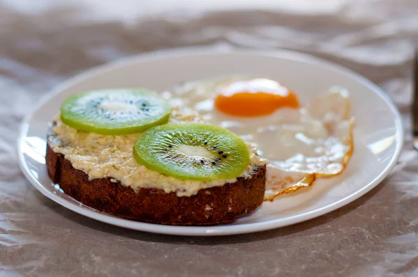 Вкусный и здоровый завтрак. Сэндвич с яичницей и киви на белой тарелке, крупный план, вид сверху и вид сбоку — стоковое фото