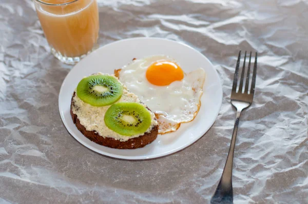 Здоровый и вкусный завтрак, сок, сэндвич с киви и яичницей на белой тарелке — стоковое фото