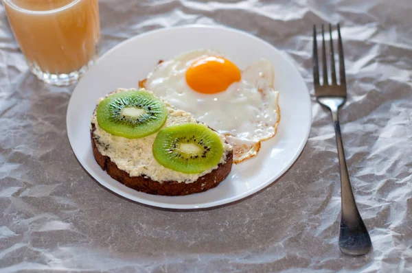 Здоровый и вкусный завтрак, сок, сэндвич с киви и яичницей на белой тарелке — стоковое фото