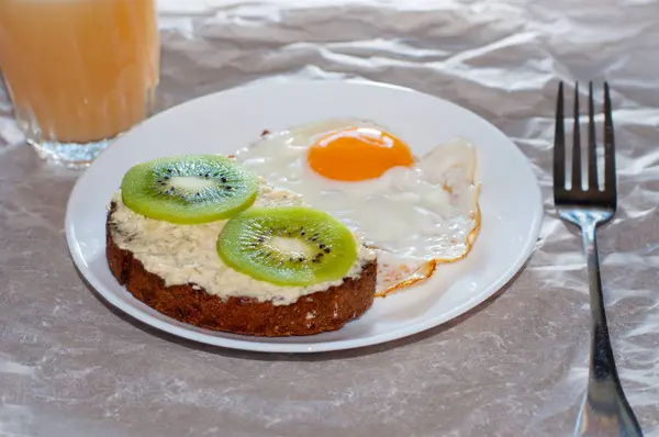 Café da manhã saudável e saboroso, suco, sanduíche integral com kiwi e ovo frito na placa branca — Fotografia de Stock