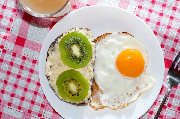 Zdravá a chutná snídaně, chinceová šťáva, celozrnný chlebový sendvič s kiwi a vajíčkem na bílé desce, růžový ubrousek — Stock fotografie