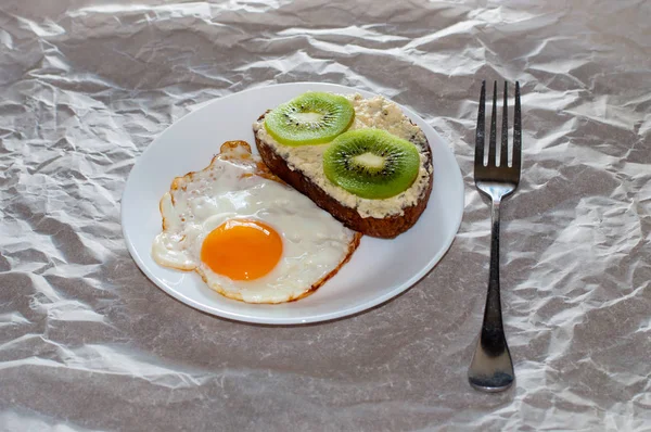 Delicioso y saludable desayuno. Huevos fritos y sándwich de kiwi en un plato blanco, primer plano, espacio para el texto — Foto de Stock