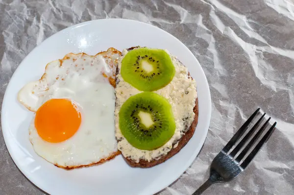 Delicioso e saudável café da manhã. Ovos fritos e sanduíche de kiwi em um prato branco, close-up, espaço para texto — Fotografia de Stock