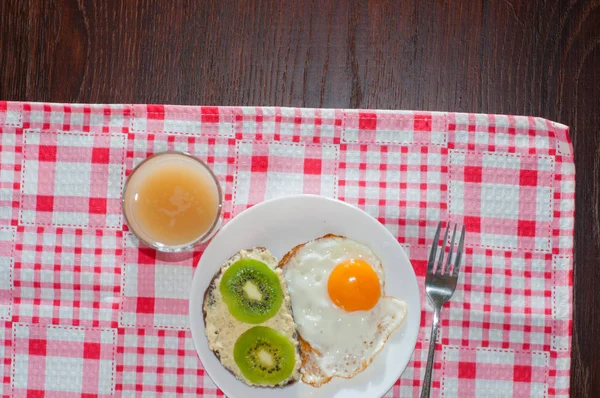 Здоровый и вкусный завтрак, айвовый сок, сэндвич с цельнозерновым хлебом с киви и яйцом на белой тарелке, розовая салфетка — стоковое фото