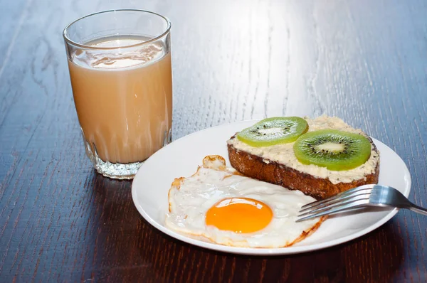 Hälsosam, välsmakande frukost, juice, fullkornsmjöl smörgås med kiwi och ett stekt ägg på en vit tallrik, på ett träbord — Stockfoto