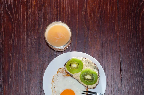Здоровый, вкусный завтрак, сок, сэндвич с хлебом из цельной муки с киви и жареным яйцом на белой тарелке, плоская кладка — стоковое фото