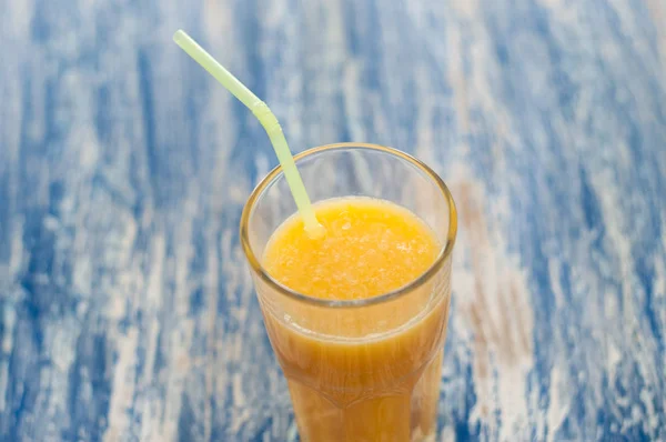 Orange juice glass with straw on a blue wooden background of sea-green, top view close-up — Stock Photo, Image