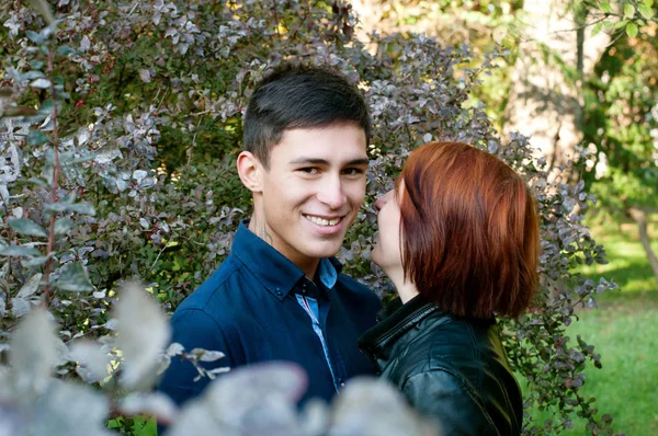 Leende, lyckliga par i kärlek, ung man och kvinna i parken. Flickan viskar i hans öra killen. — Stockfoto