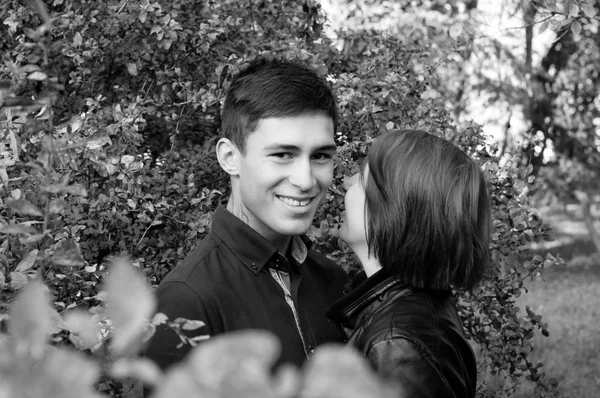 Sorrindo, casal feliz apaixonado, jovem e mulher no parque. A rapariga sussurra no ouvido dele. Retrato preto e branco dos amantes — Fotografia de Stock