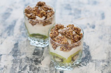 Granola, kivi, muz ve Yunan yoğurt gri beton üzerinde iki bardak, kopya alanı. Fitness, şekil, vücut ve sağlıklı gıda