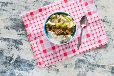 Granola Yunan yoğurt kivi ve muz ile kase de pembe bir peçete üzerinde bir kaşık, üstten görünümü, düz yatıyordu. Kilo kaybı, uygun ve lezzetli gıda için Fitness diyet