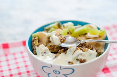 Granola yunan yoğurt kivi ve muz pembe bir peçete, yakın çekim kase ile. Kaşıkta bir parça tatlı. Kilo kaybı, uygun ve lezzetli gıda için Fitness diyet