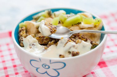 Granola yunan yoğurt kivi ve muz pembe bir peçete, yakın çekim kase ile. Kaşıkta bir parça tatlı. Kilo kaybı, uygun ve lezzetli gıda için Fitness diyet