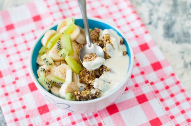 Granola Yunan yoğurt kivi ve muz pembe bir peçete üzerinde kase ile, üstten görünümü. Kaşıkta bir parça tatlı. Kilo kaybı, uygun ve lezzetli gıda için Fitness diyet