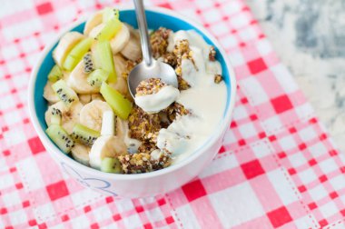 Granola Yunan yoğurt kivi ve muz pembe bir peçete üzerinde kase ile, üstten görünümü. Kaşıkta bir parça tatlı. Kilo kaybı, uygun ve lezzetli gıda için Fitness diyet