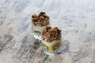 Granola, kivi, muz ve Yunan yoğurt gri beton üzerinde iki bardak, kopya alanı. Fitness, şekil, vücut ve sağlıklı gıda