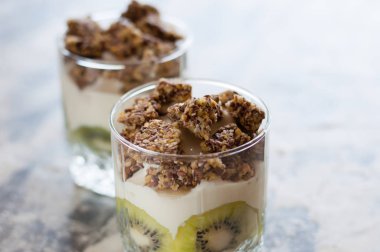 Granola, kivi, muz ve Yunan yoğurt gri beton üzerinde iki bardak, kopya alanı. Fitness, şekil, vücut ve sağlıklı gıda
