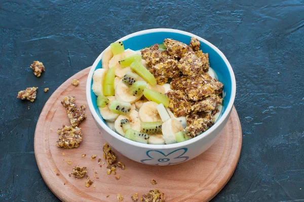 Granola, kiwi, banana and yogurt in a bowl on a wooden stand, dark background, view from the top. Fitness diet for weight loss and proper nutrition — Stock Photo, Image