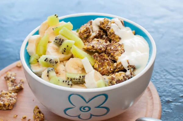 Granola, kiwi, banana and yogurt in a bowl with a spoon on a wooden stand, dark background, medium plan. Fitness diet for weight loss and proper nutrition — Stock Photo, Image