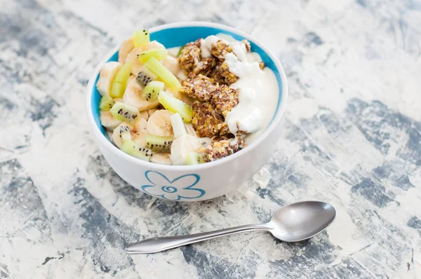 Granola, kiwi, banana and Greek yogurt in bowl with a spoon on a gray concrete background, copy space. Fitness diet for weight loss, proper nutrition and a healthy lifestyle — Stock Photo, Image