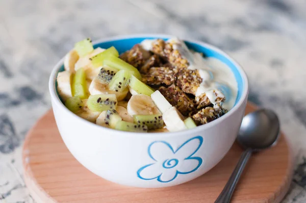 Greek yogurt, granola, kiwi and banana in a bowl on a gray concrete background, wooden tray, close-up. Fitness diet for weight loss, proper and tasty food — Stock Photo, Image