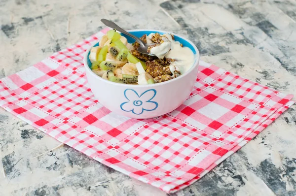 Granola with Greek yogurt kiwi and banana in bowl on a pink napkin, view from the side. Piece of dessert on a spoon. Fitness diet for weight loss, proper and tasty food