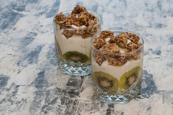 Granola, kiwi, banana and greek yogurt in glass cups on gray concrete — Stock Photo, Image