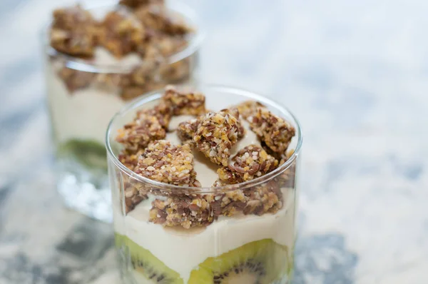 Granola, kiwi, banane et yaourt grec dans deux tasses en verre sur béton gris, espace de copie. Fitness, silhouette, corps et alimentation saine — Photo