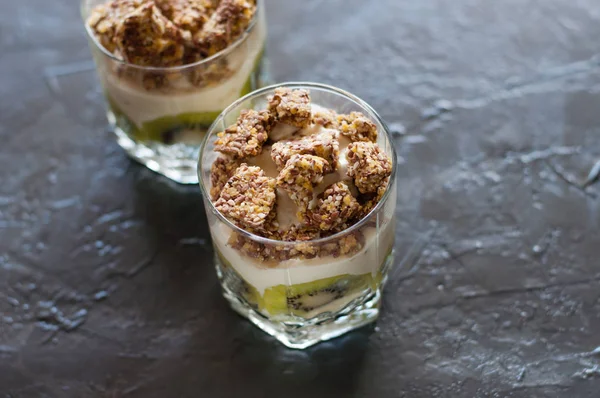 Yaourt grec, granola, banane et kiwi. Deux desserts dans des tasses en verre sur fond sombre. Concept corps et alimentation saine — Photo
