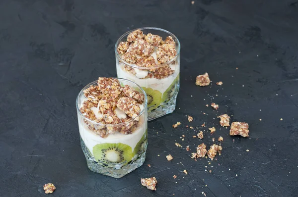 Greek yogurt, granola, banana and kiwi. Desserts in glass cups on dark background, copy space. Concept body and healthy food