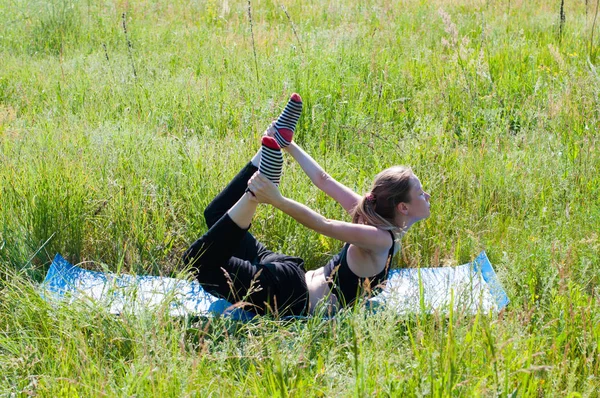 Joven hermosa mujer en un chándal hace yoga, ejercicios al aire libre en el verano medita — Foto de Stock