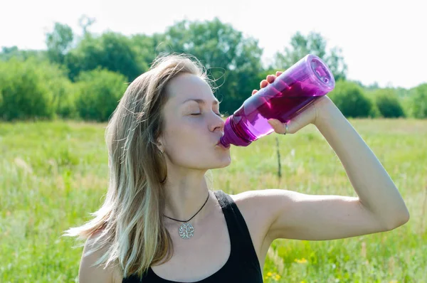 Joven hermosa mujer muy bonita en un traje deportivo bebe agua de una botella después del entrenamiento en yoga, gimnasia al aire libre en el verano —  Fotos de Stock