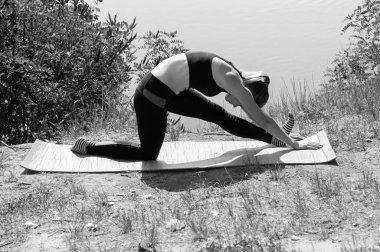 Sevimli genç kız güneşli bir yaz sabahı bir nehir, göl veya deniz kıyısında yoga asanas gerçekleştirir. Doğada diyet, egzersiz ve yoga, bw
