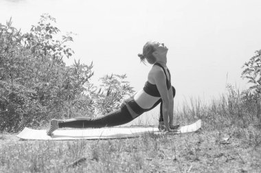 Spor plastik güzel kız nehir, göl veya deniz kıyısında yoga yapan, meditasyon, asanas bw performans