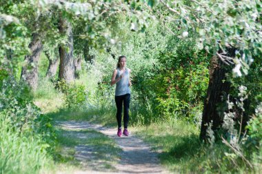 Güzel, atletik, ince kadın kulaklık ile yaz güneşli sabah parkta çalışan. Sabah koşu ve spor