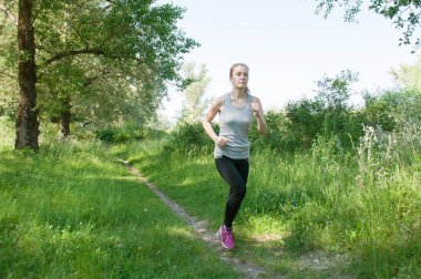 Güzel, atletik, ince kadın kulaklık ve spor takım elbise ile park, yaz, güneşli sabah çalışır. Sabah koşu ve spor