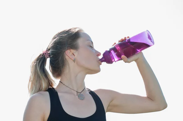 Joven hermosa mujer muy bonita en un traje deportivo bebe agua de una botella después del entrenamiento en yoga, gimnasia al aire libre en el verano —  Fotos de Stock