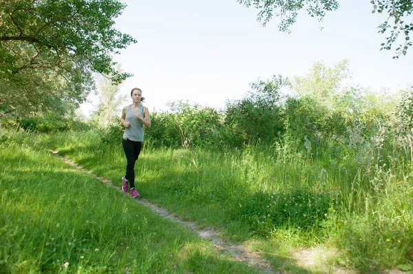 Mujer hermosa, atlética, delgada con auriculares y traje deportivo corre por el parque, verano, mañana soleada. Correr por la mañana y deportes — Foto de Stock