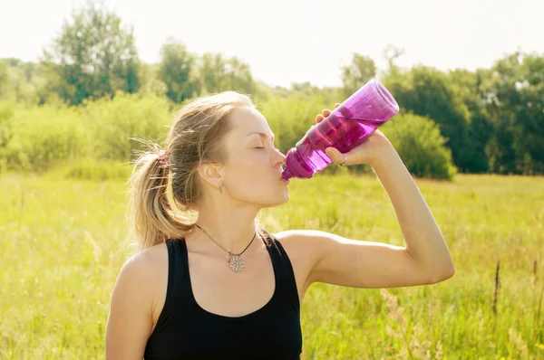 Mujer joven con una figura deportiva, cuerpo, delgado, después de un entrenamiento bebe agua de la botella —  Fotos de Stock