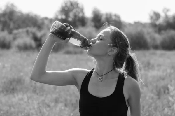 Muchacha muy hermosa bebiendo con impaciencia agua de una botella de calor, día de verano soleado, bw — Foto de Stock