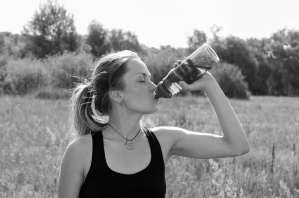 Muchacha muy hermosa bebiendo con impaciencia agua de una botella de calor, día de verano soleado, bw —  Fotos de Stock