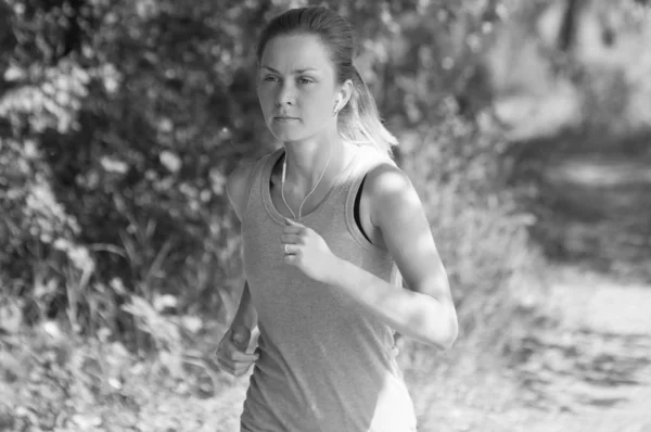 Athletic, beautiful girl runs in the park and listens to music, sunny summer morning, bw