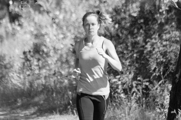 Athletic, beautiful girl runs in the park and listens to music, sunny summer morning, bw