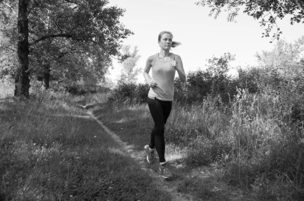 Atlética, hermosa chica corriendo en el parque o el bosque y escuchando música soleada mañana de verano, BW — Foto de Stock