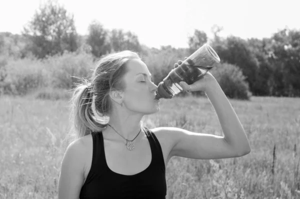 Deporte, chica bonita con ganas de beber agua de una botella en una tarde caliente en el parque, bw —  Fotos de Stock