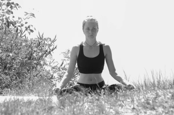 Esporte menina bonita de plástico está envolvida em ioga na margem do rio, lago ou mar, meditando, realizando asanas bw — Fotografia de Stock