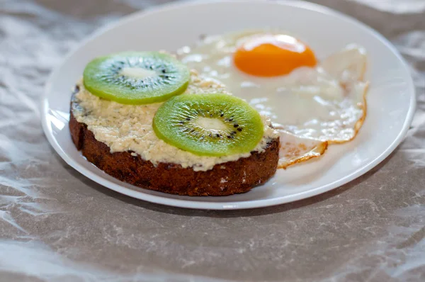 Delicioso e saudável café da manhã. Ovos mexidos e sanduíche de kiwi em um prato branco, close-up, vista superior e vista lateral — Fotografia de Stock