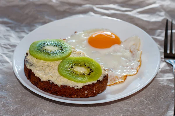 God och hälsosam frukost. Äggröra och Kiwi smörgås på en vit tallrik, närbild, uppifrån och sidovy — Stockfoto