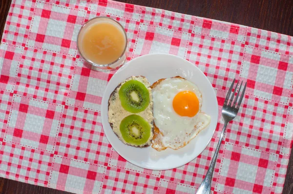 Zdravá a chutná snídaně, chinceová šťáva, celozrnný chlebový sendvič s kiwi a vajíčkem na bílé desce, růžový ubrousek — Stock fotografie